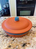 Orange ceramic casserole dish with lid and blue knob, full view