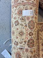Rolled ivory Persian-style rug showing multicolor floral motifs and MaxSold tag