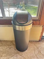 Full view of cylindrical plastic trash can with brushed metallic dome swing lid