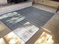 Full view of the rectangular blue and beige outdoor rug on patio surface