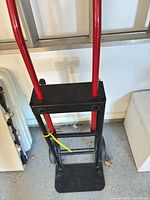 Full view of hand truck showing red handles, black frame, wheels, and fixed plate
