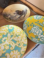 All three plates displayed: hunting scene plate and two matching floral-paisley plates