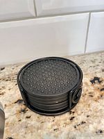 Stack of six round black coasters in holder