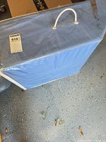 Front view of blue fabric garment storage box showing white piping, top handle and zipper closure