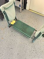 Folded garden kneeler seat on floor showing metal frame, pads and wear