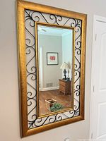 Full view of rectangular gold wood framed mirror with black metal scrollwork and inner gold liner mounted on wall