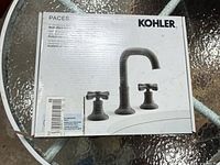 front of retail box showing Kohler Paces matte black widespread faucet image and branding