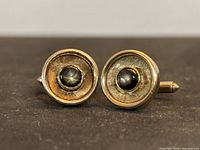 Front view of pair of yellow gold cufflinks showing brown star cabochon sapphires set in recessed textured discs