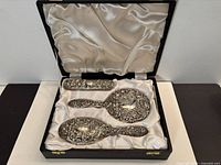 Open case showing three sterling vanity pieces seated in satin lining