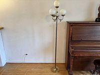 Full view of brass floor lamp beside piano, showing four globes and overall height