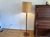 Full view of teak floor lamp beside piano