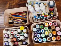 Four blush pink bins containing assorted paintbrushes, paint bottles, tubes, pens and palettes
