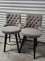 Front view of both gray tufted swivel barstools showing seats, legs, footrests
