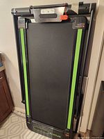Treadmill folded upright, full view of running deck with green stripes and "Sports" marking