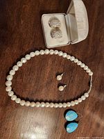 All jewelry pieces laid out: pearl necklace, pearl earrings, blue earrings, Weisfield box with pave earrings
