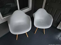 Pair of white plastic armchairs with wooden legs on porch