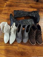 All four pairs of boots lined up: white cowboy, gray wedge, brown lace-up, black knee-high