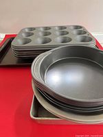 Stacked muffin tins, baking sheet and round cake pans on red surface