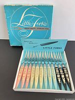 Open box showing 12 forks in rows, colored handles visible