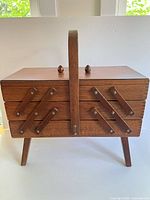 closed wooden sewing box on legs, handle visible