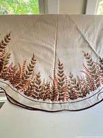 Full view showing round shape, cream fabric, fern print border, brown edge