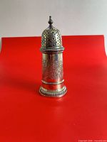 Front view of silver-plated sugar shaker against red background