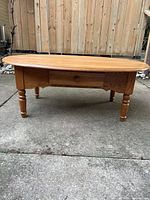 Full view of solid oak oval coffee table showing shape, legs, drawer front