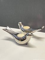 Two chrome bird tealight holders with candles inserted