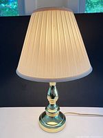 Lamp illuminated showing brass base and pleated shade