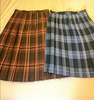 Two tartan pleated skirts laid flat showing full patterns and pleats