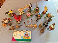 Full group shot of eight Lenox bird figurines, four metal spoons, bird book
