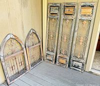 Five shutters leaning against wall: three tall rectangular, two arched