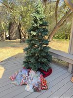 Full view of artificial Christmas tree with tree skirt and bagged ornaments at base