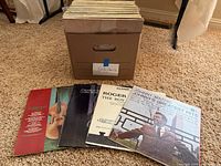 Box of LPs with several records displayed in front showing covers
