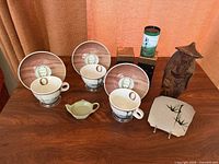 Full lot overview showing three cup-and-saucer sets, wood figurine, two tins, creamer, square plate