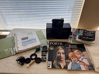 Overview of camera, box, batteries, caps, charger, cleaning tools, books and envelopes on table