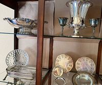 Full cabinet view showing all silver-plated pieces including compote bowl, urn, goblets, plates, coasters, tray with glass insert
