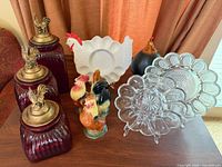 Group view of all items: red glass canisters, clear plates, white hen plate, ceramic roosters, black rooster