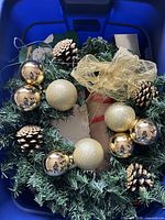 Wreath with gold ornaments, gold bow and pinecones in bin