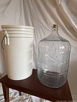 Glass carboy next to white plastic bucket
