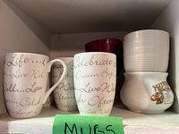 Shelf with two script text mugs, red mug, stack of white bowls and Mush mug