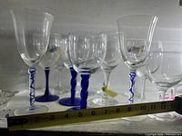 Front view of assorted wine glasses showing blue twisted stems and clear variants with tape measure for scale