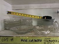 Overall lot on shelf showing bowls, plate, juicer with tape measure for scale