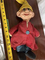 Full doll next to tape measure showing approx. 15 in height, red coat, yellow hat