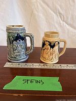 Both steins side by side with ruler for scale