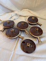 Five brown glazed bowls each with lid displayed on cloth backdrop