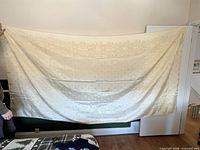 Full view of the ivory damask tablecloth held up to show size and pattern