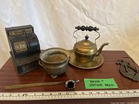 Group view showing toy register, brass teapot on tray, brass pot, trivet, brass rod, spoon, fittings