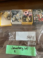 Four trays of assorted costume jewelry pieces in front of labeled Ziploc bag