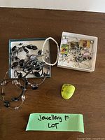 Overview of mixed jewelry items on table: necklaces, bracelets, green stone, box of charms